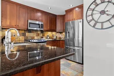 a kitchen with wooden cabinets and a stainless steel refrigerator at Mountain Views Lux 2BR Condo in Canmore with Hot Tub in Canmore