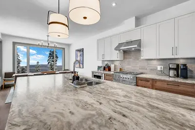 a kitchen with white cabinets and a large marble counter top at Western Star Chalet Ski in out and Amazing Mtn View in Big White