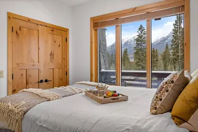 a bedroom with a large bed with a large window at Luxurious Condo Mountain Views Hot-tub and Billiards in Canmore