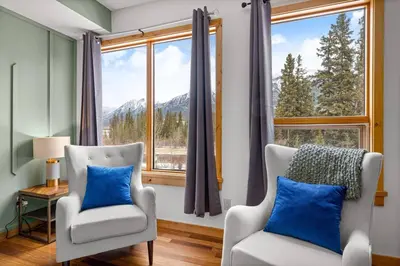 a living room with two chairs and a large window at Luxurious Condo Mountain Views Hot-tub and Billiards in Canmore