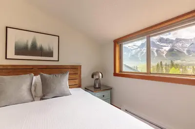 a bedroom with a bed and a window with mountains at Cloud Nine - Stunning Views Rooftop Hot Tub in Canmore