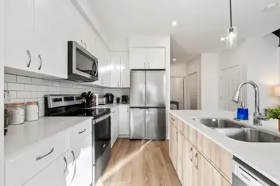 a kitchen with white cabinets and a stainless steel refrigerator at Luxe Retreat with Gym, Ping Pong, King Bed, Near WEM in Edmonton