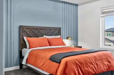 a bedroom with a bed with an orange comforter and a window at Spacious 4 Beds Sleeps 8 Near Airport Family Home in Nisku
