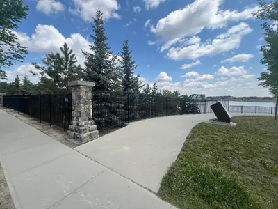 a sidewalk with a wrought iron fence and a bench at Deluxe Mahogany Lake Getaway Sleeps 4 in Calgary