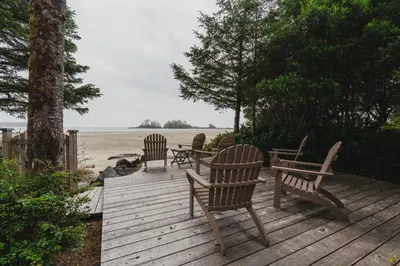 three wooden chairs sitting on a wooden deck near the beach at Chesterman on the Point - Beachfront in Tofino