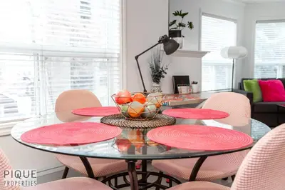 a dining room with a glass table and pink chairs at The Neon Palace - King Bed - Fireplace - Netflix - UGPark in Edmonton