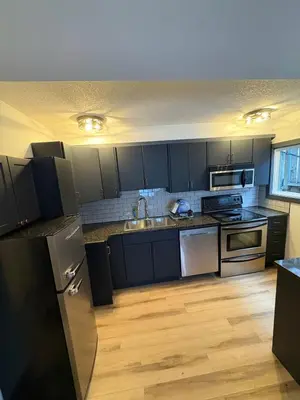 a kitchen with black cabinets and stainless steel appliances at Cozy boho downtown apartment in Calgary