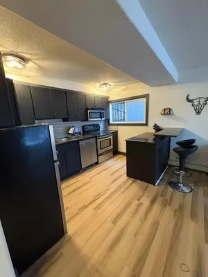 a kitchen with black cabinets and a wooden floor at Cozy boho downtown apartment in Calgary