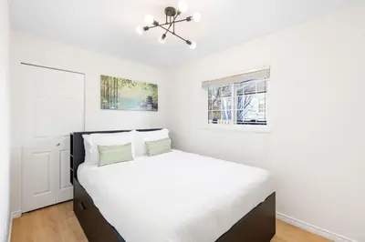 a white bedroom with a bed and a window at NEW Roomy 3BR Family Suite. 5 min to Skytrain. in Vancouver