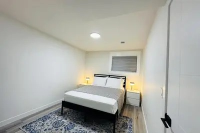 a white bedroom with a bed and a blue rug at Brand New cozy apartment bright, modern private 2 bedroom basement! in Calgary