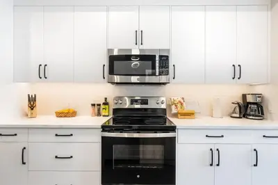 a kitchen with white cabinets and a black stove top oven at Brand New 2BR Oasis Mins to DT with AC Balcony and BBQ in Golden