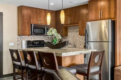 a kitchen with wooden cabinets and a stainless steel refrigerator at Cozy Rocky Mountain Studio with Hot tub and Gym in Canmore