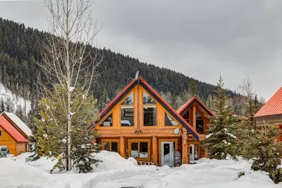 a log cabin with snow in front of a mountain at Beautiful Rustic Chalet in the Heart of Rockies in Golden