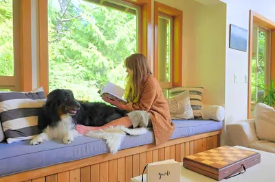 a woman sitting on a window seat with a dog at Cedar and Salt in Tofino