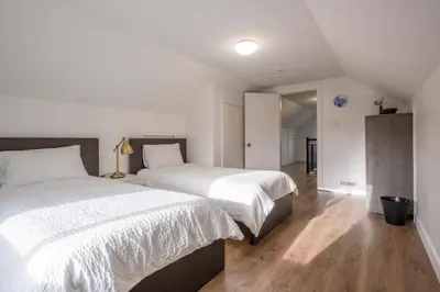 a bedroom with two beds with white sheets and wood floors at Quiet 5 BR 7 bed Escape with sunny Deck near UBC in Vancouver