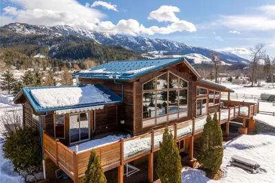 a log home in the snow with mountains in the background at Elk River Estate by Fernie Central Reservations in Fernie