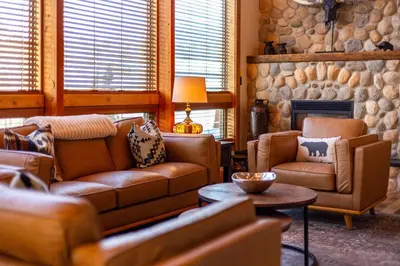 a living room with leather furniture and a stone fireplace at Elk River Estate by Fernie Central Reservations in Fernie