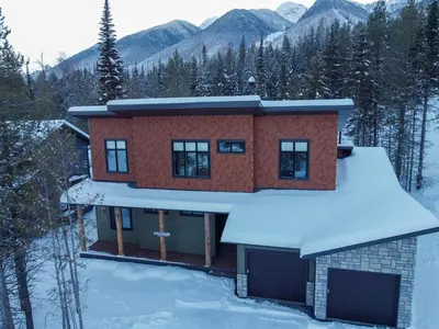 a house in the snow with mountains in the background at Moose Lodge by Fernie Central Reservations in Fernie