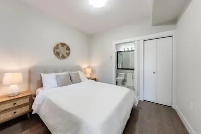 a white bedroom with a large bed and a bathroom at Private Entrance Suite Near Deer Lake & Metro in Burnaby