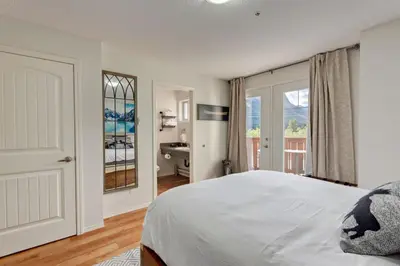 a white bedroom with a bed and a bathroom at Charming Condo In The Heart Of Canmore in Canmore