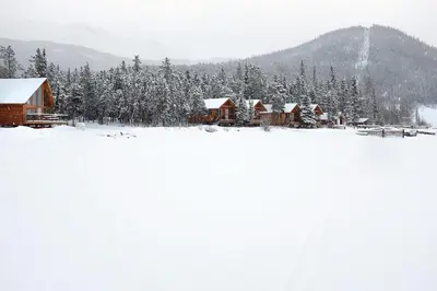 a group of wooden cabins in a snow covered forest at Northern Rockies Lodge in Muncho Lake