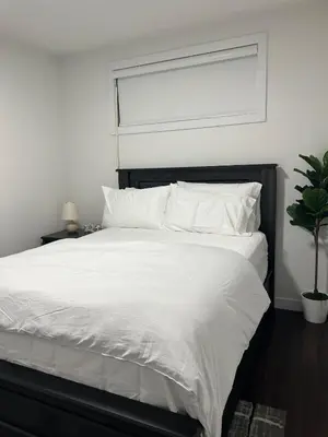 a bedroom with a bed with white sheets and a window at Kizito in Edmonton