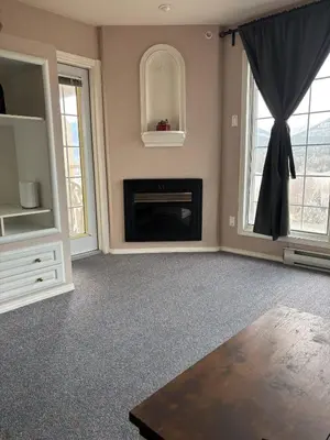 a living room with a fireplace and two windows at Cozy getaway with a view! in Fairmont Hot Springs