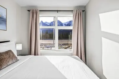 a bedroom with a bed and a window with mountains at 3BR Rockies Haven Near Banff with Private Patio in Canmore