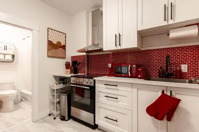 a kitchen with white cabinets and a red brick wall at Retro-Chic Hideaway - Walking Distance To Stampede in Calgary