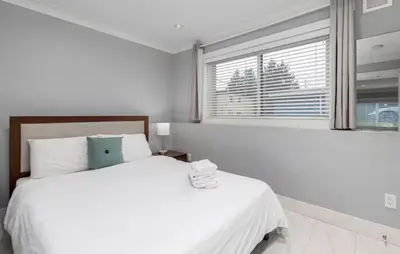 a white bedroom with two beds and a window at Large 3 Bedroom Laneway House in Vancouver