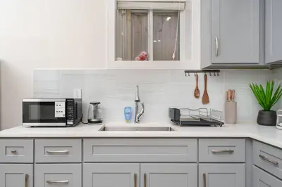 a white kitchen with a sink and a microwave at New Modern 2BR Suite near UBC Pacific Spirit Park in Vancouver