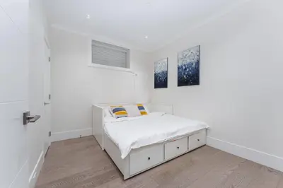 a white bedroom with a bed and two paintings at New Modern 2BR Suite near UBC Pacific Spirit Park in Vancouver
