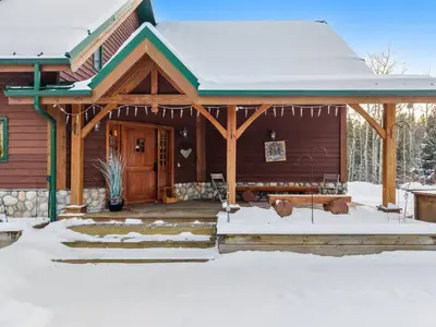 a log cabin with snow on the porch at Highlands Homestead Luxury Retreat in Bragg Creek