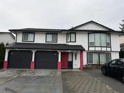 a white house with two garage doors and a car at J & J Dream Villa Ltd in Abbotsford