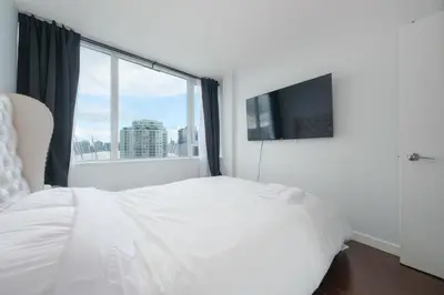 a bedroom with a white bed and a large window at Cozy Condo in Prime Location with Jacuzzi Pool & Sauna in Vancouver