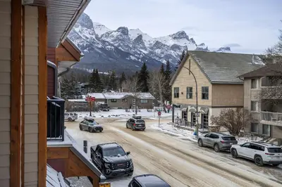 a street in a town with a snow covered mountain at Heart of Canmore Condo managed by Little Sister Getaways in Canmore