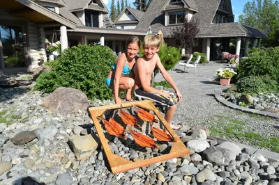 a boy and a girl sitting next to a fire grill at Retreat Wilderness Inn in Nimpo Lake