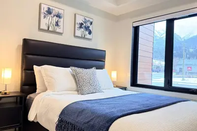 a bedroom with a large bed with a large window at Canmore Peaks Retreat | Luxe 1BR w Pool & Gym in Canmore