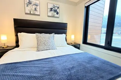 a bedroom with a bed with a blue comforter and two windows at Canmore Peaks Retreat | Luxe 1BR w Pool & Gym in Canmore