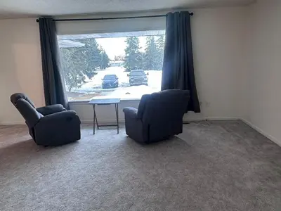 a living room with two chairs and a table and a window at Cozy West Edmonton Home Near Jasper Park & shops in Edmonton