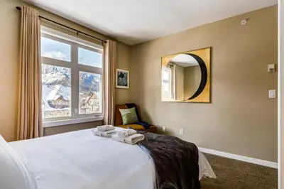 a bedroom with a bed with a mirror and a window at Stylish Mountain View Condo with Gym in Canmore