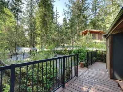 a wooden deck with a black fence and trees at Hot Tub - Pet Friendly - Cozy Escape with Fire Pit in Port Renfrew