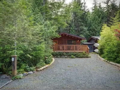 a cabin in the woods with a gravel driveway at Enclosed deck - Hot tub - Pet Friendly- gas stove in Port Renfrew
