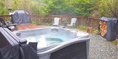 a hot tub in a yard with chairs and a fence at A slice of paradise with Hot Tub - Pet Friendly in Port Renfrew