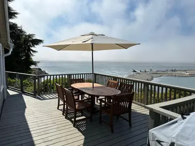 a table with an umbrella on a deck with the beach at Hot tub - Sauna - Panoramic Ocean View THE POINT - Pet Friendly in Port Renfrew
