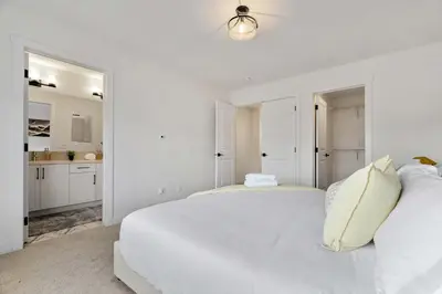 a white bedroom with a bed and a kitchen at NEW Family 3BR Upper Suite w Kid's Play Den, Free Banff Pass in Calgary
