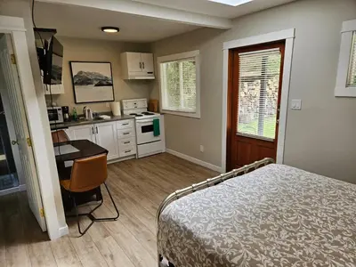 a bedroom with a bed and a desk and a kitchen at Cozy Rainforest Cottage for 2 - Pet Friendly in Port Renfrew