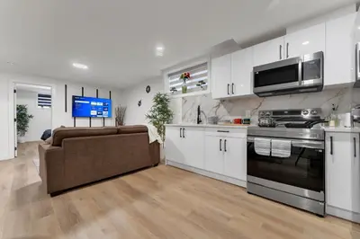 a kitchen with white cabinets and a couch and a tv at 2-bedroom suite close to Amenities and Airport with on pad parking in Leduc