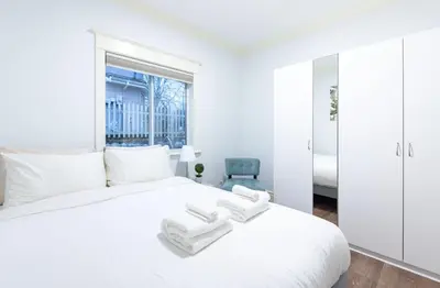 a white bedroom with a white bed and a blue chair at 3Beds Ground-Level Private Suite in Burnaby in Burnaby