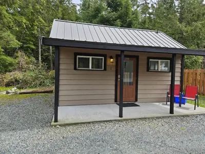 a small shed with a door and a chair at Rustic Rainforest Cabin for 2 - Peaceful - Pet Friendly in Port Renfrew